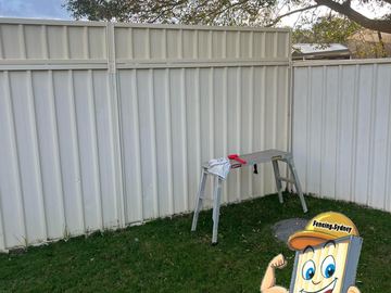 Cream Colorbond privacy fence on a lawn with a step stool standing in front