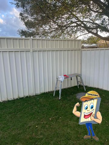 Cream Colorbond privacy fence on a lawn with a step stool standing in front