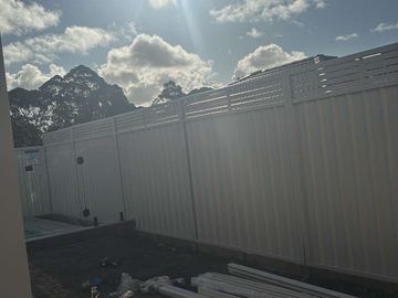 Mid grey Colorbond privacy fence with a slat height extension under a cloudy sky