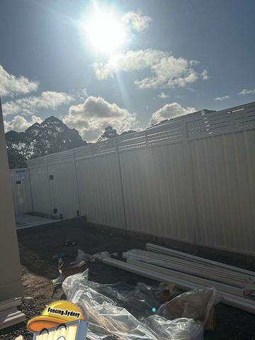 Mid grey Colorbond privacy fence with a slat height extension under a cloudy sky