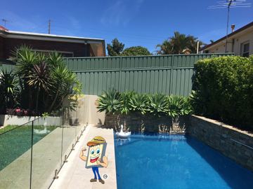 Cream Colorbond privacy fence beside a glass pool fence and tropical plants