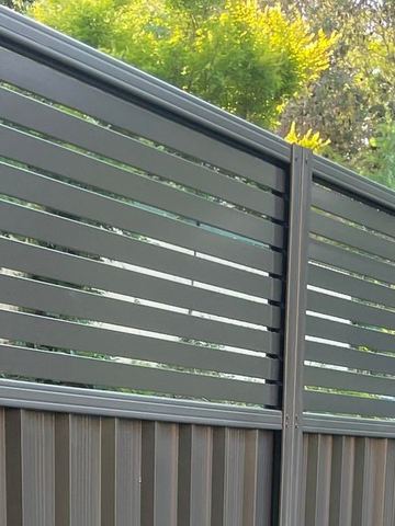 Charcoal Colorbond fence with an open horizontal slat topper along a garden boundary