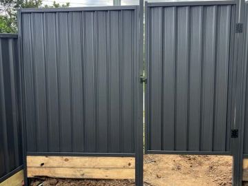 Charcoal gate and panel mount on double timber sleepers over bare soil with latch hardware visible.