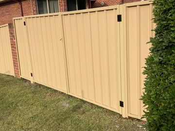 Cream Colorbond pedestrian gate set in a matching fence beside garden hedging