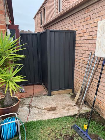 Charcoal Colorbond pedestrian gate set in a brick alcove beside a potted plant