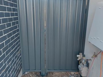 Close view of a mid grey Colorbond pedestrian gate beside conduit and a meter box