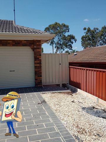 Cream side gate meets long terracotta-brown panels on grey concrete sleepers above white gravel and paver drive.