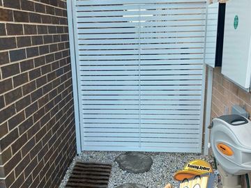 White slat gate on gravel and stepping stones closes a side passage between dark and light brick walls.