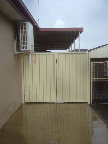 The scene shows a mid grey corrugated steel fence where a gate sits in the run, sleepers form the base.