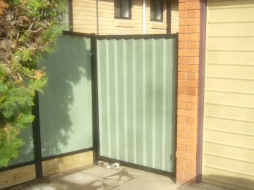 The scene shows a green corrugated steel fence where a gate sits in the run, sleepers form the base.