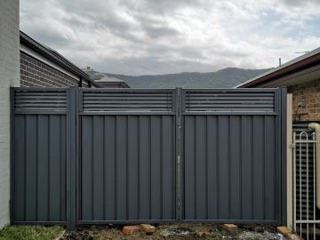 Charcoal panels with louvre tops include a double swing gate set between brick houses on rough ground.