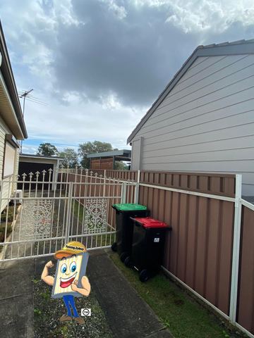 Cream Colorbond privacy fence with a white mesh side gate beside wheelie bins