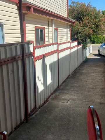 Cream corrugated sheets in heritage-red frames step along a concrete side drive beside weatherboard cladding.