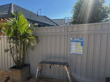 Cream Colorbond privacy fence with a potted palm and a step stool on a paved courtyard