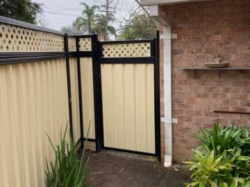 Cream Colorbond pedestrian gate with a lattice top in a black frame beside a brick wall