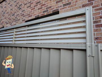 Close view of a cream Colorbond fence with a slat topper against a brick wall