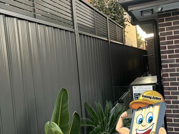 Charcoal Colorbond privacy fence with a slat height extension meeting a brick house