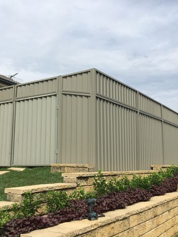 The scene shows a light grey corrugated steel fence where an upper infill raises the height, sleepers form the base.