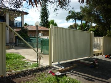 The scene shows a mid grey corrugated steel fence where a gate sits in the run, sleepers form the base.