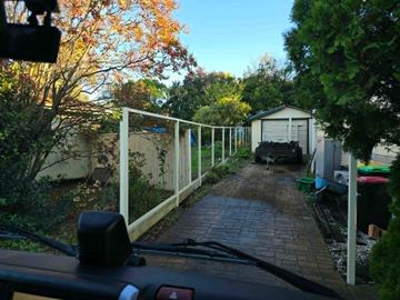 White tubular fence running beside a paved path toward a backyard shed