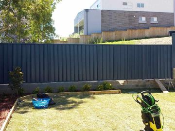 Dark Colorbond privacy fence on a timber edge beside a lawn and garden mower