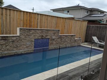 Timber paling fence behind a swimming pool and a stone feature wall