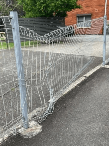 Crushed galvanised mesh panel sagging beside an asphalt driveway