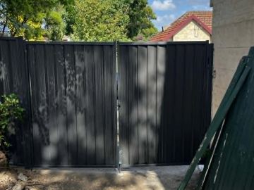 Black Colorbond double driveway gate beside a rendered wall