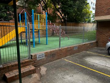 Silver weldmesh with rolled edges caps a brick retaining wall around synthetic turf, a yellow slide and visitor parking signs.