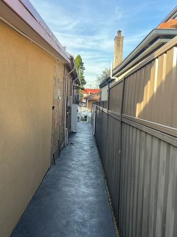 Mid grey Colorbond privacy fence running along a paved side passage beside a cream garage wall