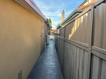 Mid grey Colorbond privacy fence running along a paved side passage beside a cream garage wall