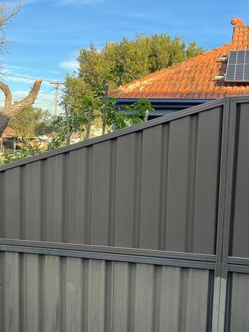 Charcoal Colorbond privacy fence stepping up a slope beside a white gate post