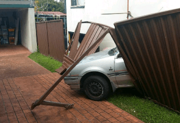Crumpled chocolate corrugated fencing lies across a brick driveway where a silver car pushed through the boundary.