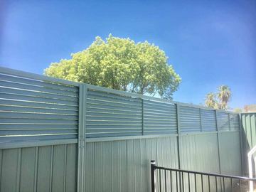 Light green corrugated lower sections pair with louvre tops above black tubular fencing under a clear sky.