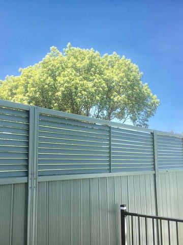 Light green corrugated lower sections pair with louvre tops above black tubular fencing under a clear sky.
