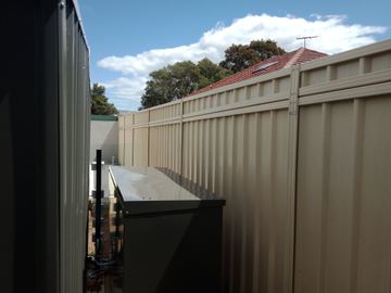 Cream Colorbond privacy fence running beside a black backyard shed