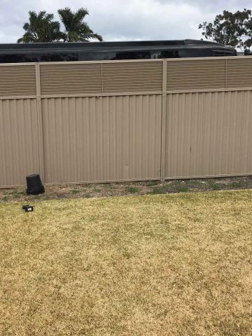 The scene shows a mid grey corrugated steel fence where an upper infill raises the height, sleepers form the base.