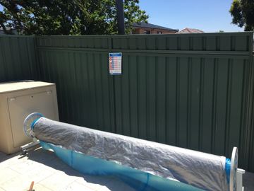 Green Colorbond privacy fence beside a rolled pool cover and a white equipment box