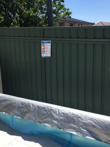 Green Colorbond privacy fence beside a rolled pool cover and a white equipment box