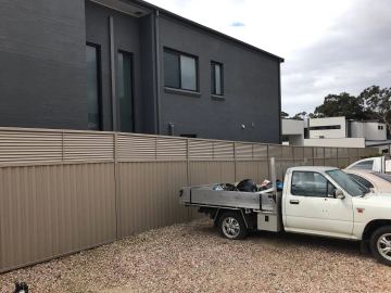 The scene shows a mid grey corrugated steel fence where an upper infill raises the height, sleepers form the base.