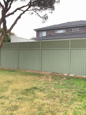 The scene shows a mid grey corrugated steel fence where louvre sections add ventilation, sleepers form the base.