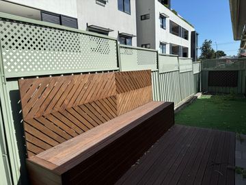 Pale Colorbond fence with a lattice topper beside a timber bench on a deck
