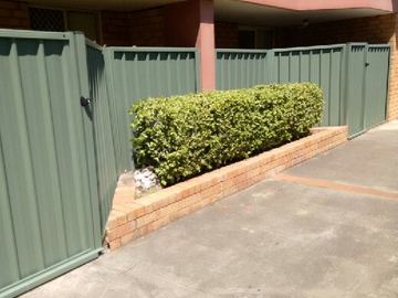 The scene shows a mid grey corrugated steel fence where sleepers form the base.