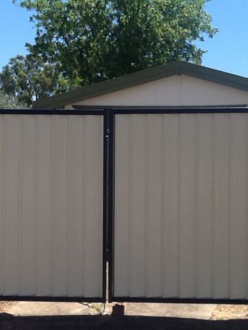 The scene shows a mid grey corrugated steel fence where concrete paving runs alongside.