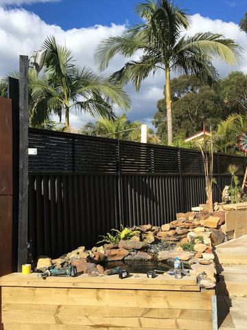 The scene shows a mid grey corrugated steel fence where an upper infill raises the height, sleepers form the base.