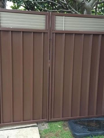 The scene shows a charcoal corrugated steel fence where residential buildings appear beyond the line.