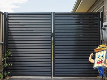The scene shows a mid grey corrugated steel fence where a gate sits in the run, louvre sections add ventilation, concrete paving runs alongside.
