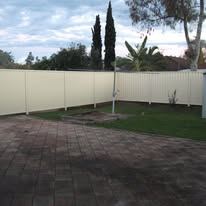 Cream Colorbond fence around a paved yard