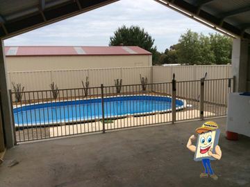 Cream tubular panels and gate enclose a blue above-ground pool beside cream corrugated fencing and a shed roof.