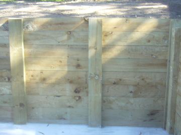 Horizontal treated pine sleepers bolted to vertical posts turn a clean corner above a white concrete edge.